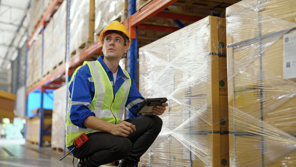 Warehouse operations manager inspecting palletized inventory during a WMS implementation using a mobile device to verify data accuracy and processes.