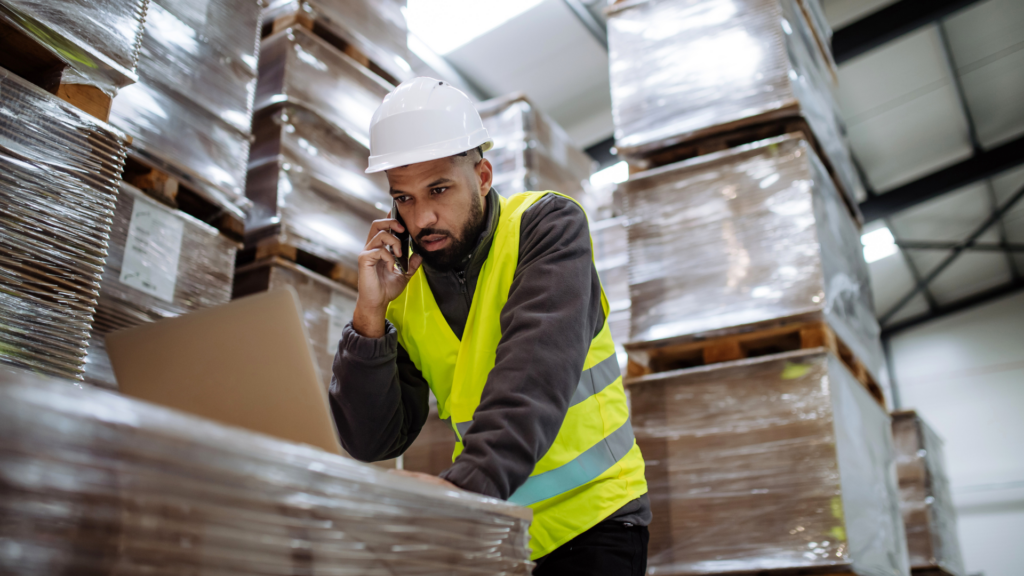 Warehouse manager coordinating a WMS upgrade rollout by phone and laptop